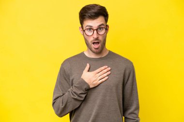 Sarı arka planda izole edilmiş genç beyaz adam sağa bakarken şaşırdı ve şok oldu.