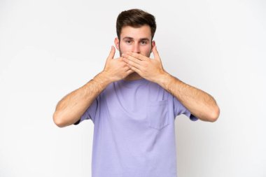 Beyaz arka planda izole edilmiş genç beyaz bir adam elleriyle ağzını kapatıyor.
