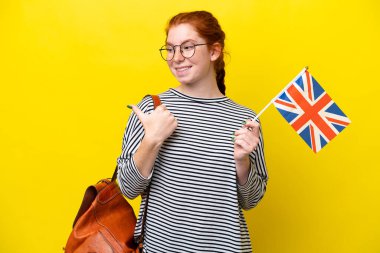 Sarı arka planda Birleşik Krallık bayrağı taşıyan İspanyol genç bir kadın bir ürünü sunmak için kenarı işaret ediyor.