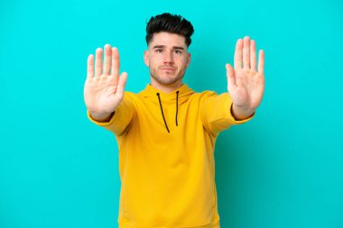 Mavi arka planda izole edilmiş genç beyaz adam dur hareketi yapıyor ve hayal kırıklığına uğruyor.