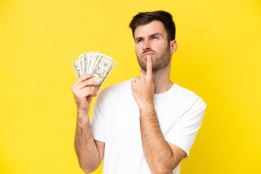 Kafkasyalı genç adam sarı arka planda izole edilmiş bir sürü para alıyor.