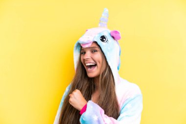 Sarı arka planda izole edilmiş tek boynuzlu at pijaması giyen beyaz bir kadın zaferi kutluyor.