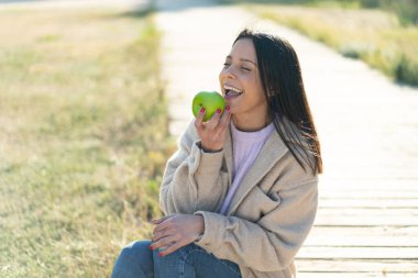 Dışarıda elinde elma tutan genç bir kadın.
