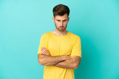 Mutsuz bir ifadeyle mavi arka planda izole edilmiş beyaz, yakışıklı genç bir adam.