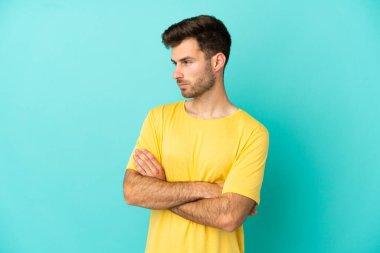 Mavi arka planda izole genç beyaz adam kollarını çapraz tutuyor.