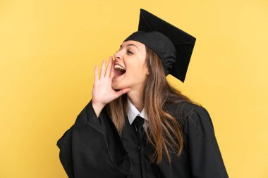 Sarı arka planda izole edilmiş genç üniversite mezunu ağzı sonuna kadar açık bağırıyor.