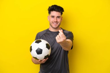 Yakışıklı genç futbolcu sarı arka planda izole edilmiş para hareketi yapıyor.