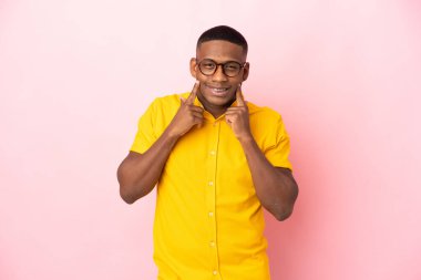 Genç Latin bir adam pembe arka planda izole edilmiş mutlu ve hoş bir ifadeyle gülümsüyor.
