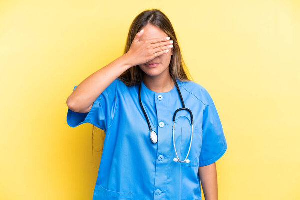 Young nurse caucasian woman isolated on yellow background covering eyes by hands. Do not want to see something