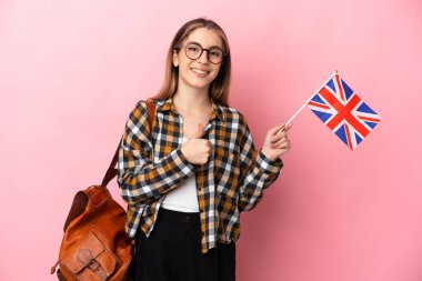 Birleşik Krallık bayrağını tutan genç İspanyol kadın pembe arka planda izole edilmiş bir şekilde baş parmak işareti yapıyor.