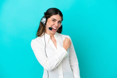 Tele pazarlamacı İtalyan kadın mavi arka planda izole edilmiş bir kulaklıkla çalışarak zaferi kutluyor.