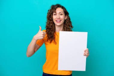 Young caucasian woman isolated on blue background holding an empty placard with thumb up