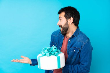 İzole edilmiş mavi arkaplanı olan büyük pastası olan yakışıklı genç bir adam.
