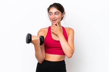 Beyaz arka planda halter kaldıran genç beyaz kadın yan tarafa bakıyor ve gülümsüyor.