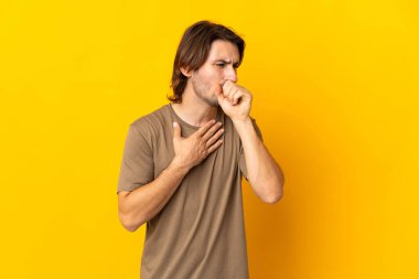 Sarı arka planda izole edilmiş genç yakışıklı adam çok öksürüyor.