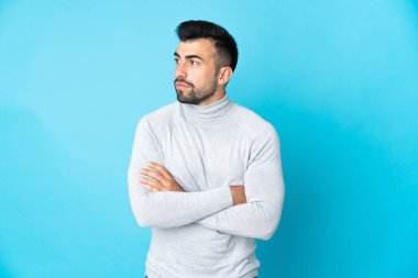 İzole edilmiş mavi arka planda beyaz bir adam yan tarafa bakıyor.