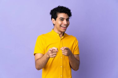 Genç Venezuelalı adam mor arka planda izole edilmiş, şaşırmış ve ön tarafı işaret ediyor.