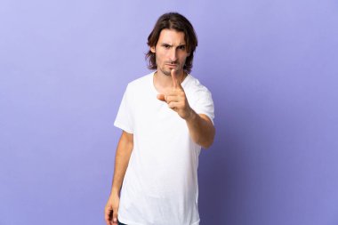 Mor arka planda izole edilmiş genç yakışıklı hayal kırıklığına uğramış ve ön tarafı işaret ediyor.