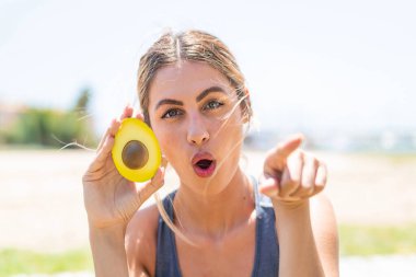 Avokado tutan genç sarışın kadın şaşırmış ve ön tarafı işaret ediyor.