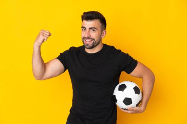 İzole edilmiş sarı arka planda, futbol topu zaferi kutlayan beyaz bir adam.