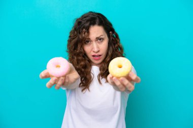 Kafkasyalı genç bir kadın mavi arka planda izole edilmiş elinde donut ve üzgün