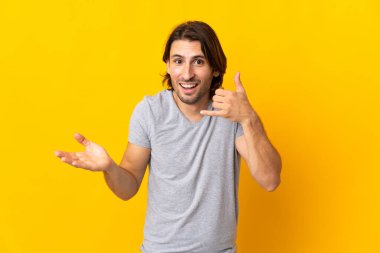 Sarı arka planda izole edilmiş genç yakışıklı bir adam telefon jesti yapıyor ve şüpheleniyor.