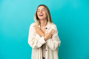 İzole edilmiş mavi arka planda genç bir kadın gülümsüyor ve zafer işareti gösteriyor