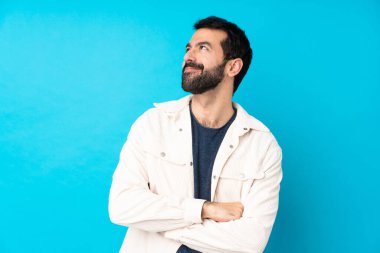 Mavi arka planda beyaz kadife ceketli yakışıklı genç adam gülümserken yukarı bakıyor.