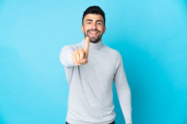İzole edilmiş mavi arka plan üzerinde beyaz bir adam parmağını kaldırıyor ve gösteriyor.