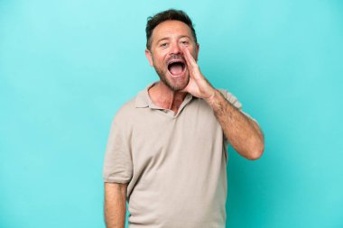 Orta yaşlı beyaz bir adam mavi arka planda izole edilmiş, şaşırmış ve şok olmuş bir yüz ifadesi var.