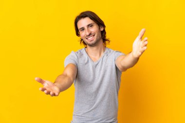 Sarı arka planda soyutlanmış genç yakışıklı adam sunar ve davet eder.