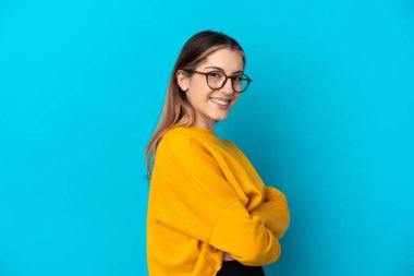 Mavi arka planda soyutlanmış genç beyaz kadın yana bakıyor ve gülümsüyor.