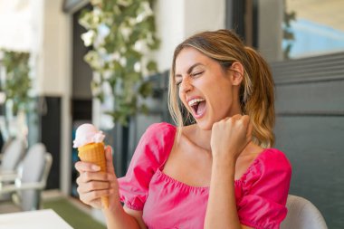 Açık havada kornet dondurmalı genç sarışın kadın zaferi kutluyor.