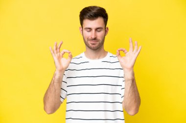 Zen pozisyonunda sarı arka planda izole edilmiş genç beyaz adam.