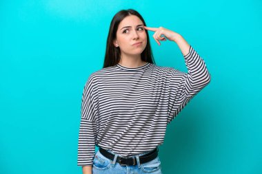 Kafkasyalı genç bir kadın mavi arka planda izole edilmiş. Delilik jesti yapıyor. Parmağını kafaya koyuyor.
