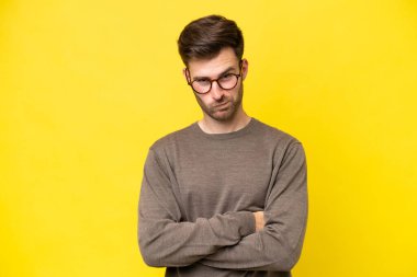Mutsuz bir ifadeyle sarı arka planda izole edilmiş genç beyaz bir adam.