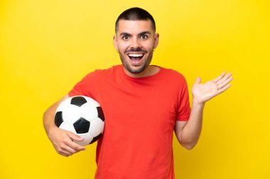 Futbol oynayan beyaz bir adam sarı arka planda izole edilmiş, şok olmuş bir yüz ifadesi var.