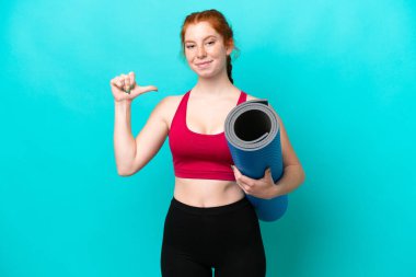 Kırmızı spor yapan genç bir kadın yoga derslerine giderken elinde mavi arka planda kendini beğenmiş ve gururlu bir minder tutuyordu.