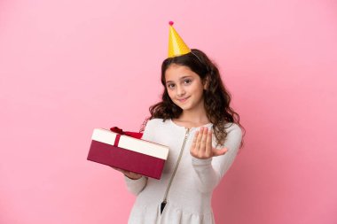 Küçük beyaz kız pembe arka planda izole edilmiş bir hediye tutuyor. Bizimle gelmesi için davet ediyor. Gelmene sevindim.