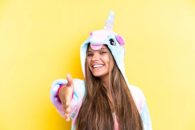 Sarı arka planda izole edilmiş tek boynuzlu at pijaması giyen beyaz bir kadın iyi bir anlaşma için el sıkışıyor.