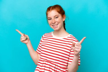 Mavi arka planda izole edilmiş genç, kırmızı bir kadın parmak uçlarını işaret ediyor ve mutlu.