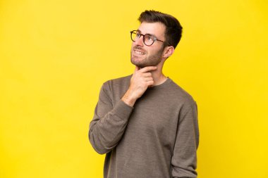 Sarı arka planda izole edilmiş genç beyaz adam gülümserken yukarı bakıyor.