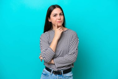 Kafkasyalı genç bir kadın mavi arka planda izole edilmiş ve düşünüyor