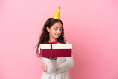 Küçük beyaz kız pembe arka planda üzgün bir ifadeyle izole edilmiş bir hediye tutuyor.