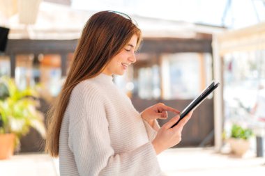 Genç beyaz kadın tablet ekranına mutlu bir ifadeyle dokunuyor.