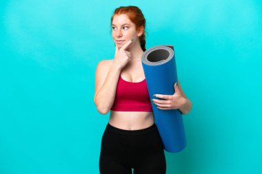 Genç spor kırmızısı kadın yoga derslerine giderken elinde mavi arka planda bir minder tutarken kuşkuları vardı.