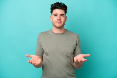 Mavi arka planda izole edilmiş genç beyaz adam mutlu ve gülümsüyor.