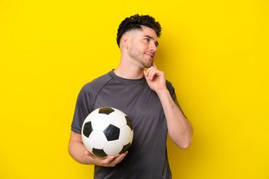 Yakışıklı genç futbolcu sarı arka planda izole edilmiş bir şekilde yukarı bakarken bir fikir düşünüyor.