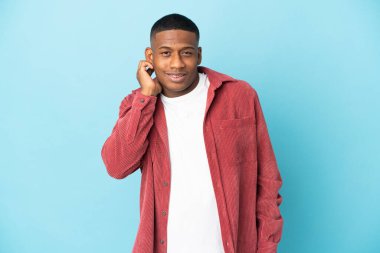 Genç latin adam mavi arka planda yalnız gülüyor.