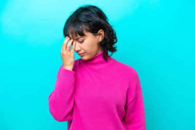 Genç Arjantinli kadın mavi arka planda başağrısı ile izole edilmiş.